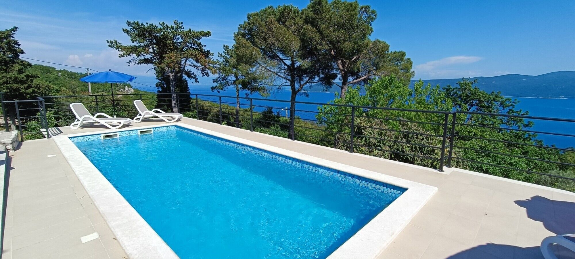 A rectangular swimming pool with clear blue water, surrounded by a tiled deck.