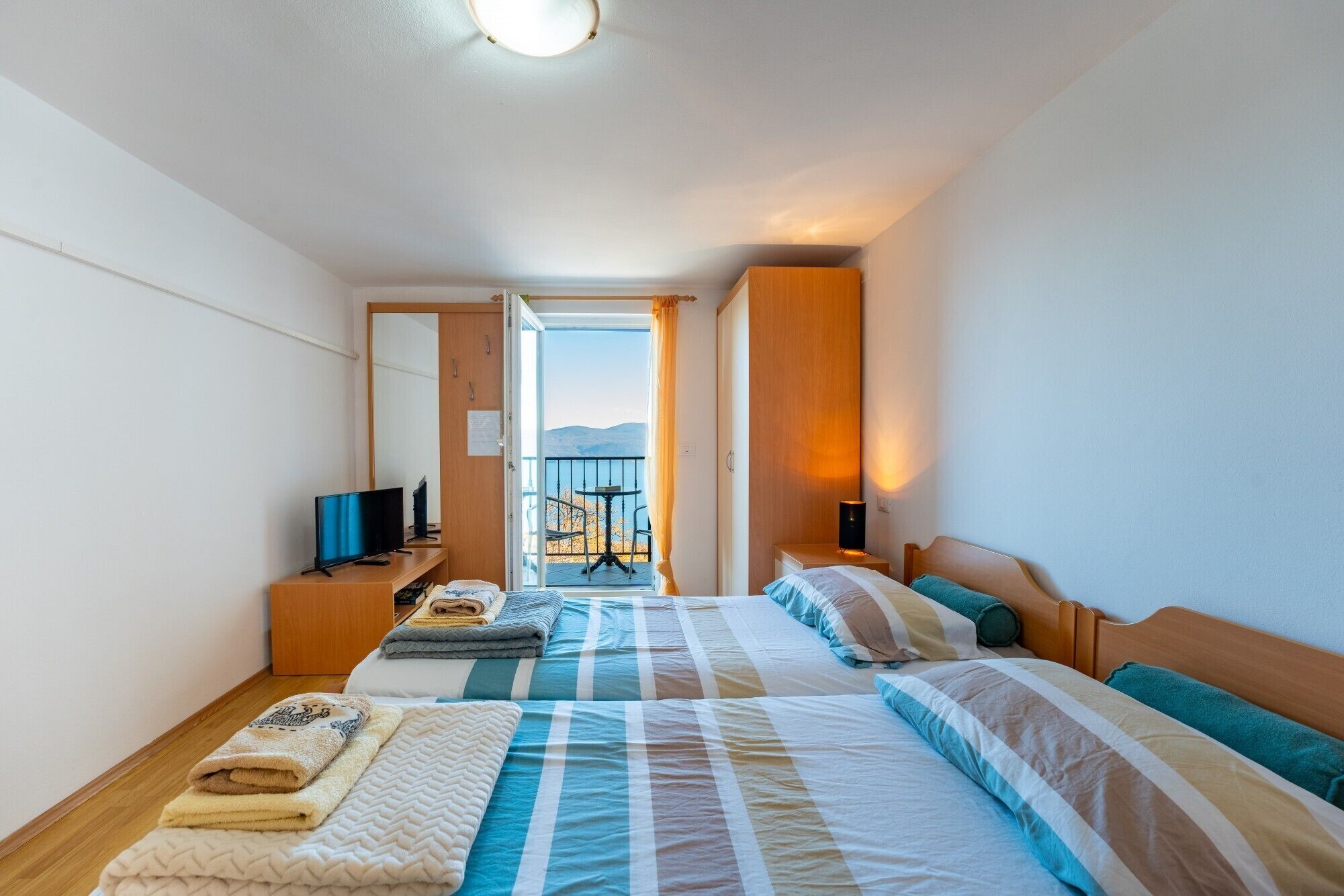 Habitación de hotel con dos camas, televisor, escritorio y balcón con vistas.