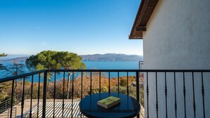 A balcony with a view of a lake and mountains, a round table with a book, and a railing.