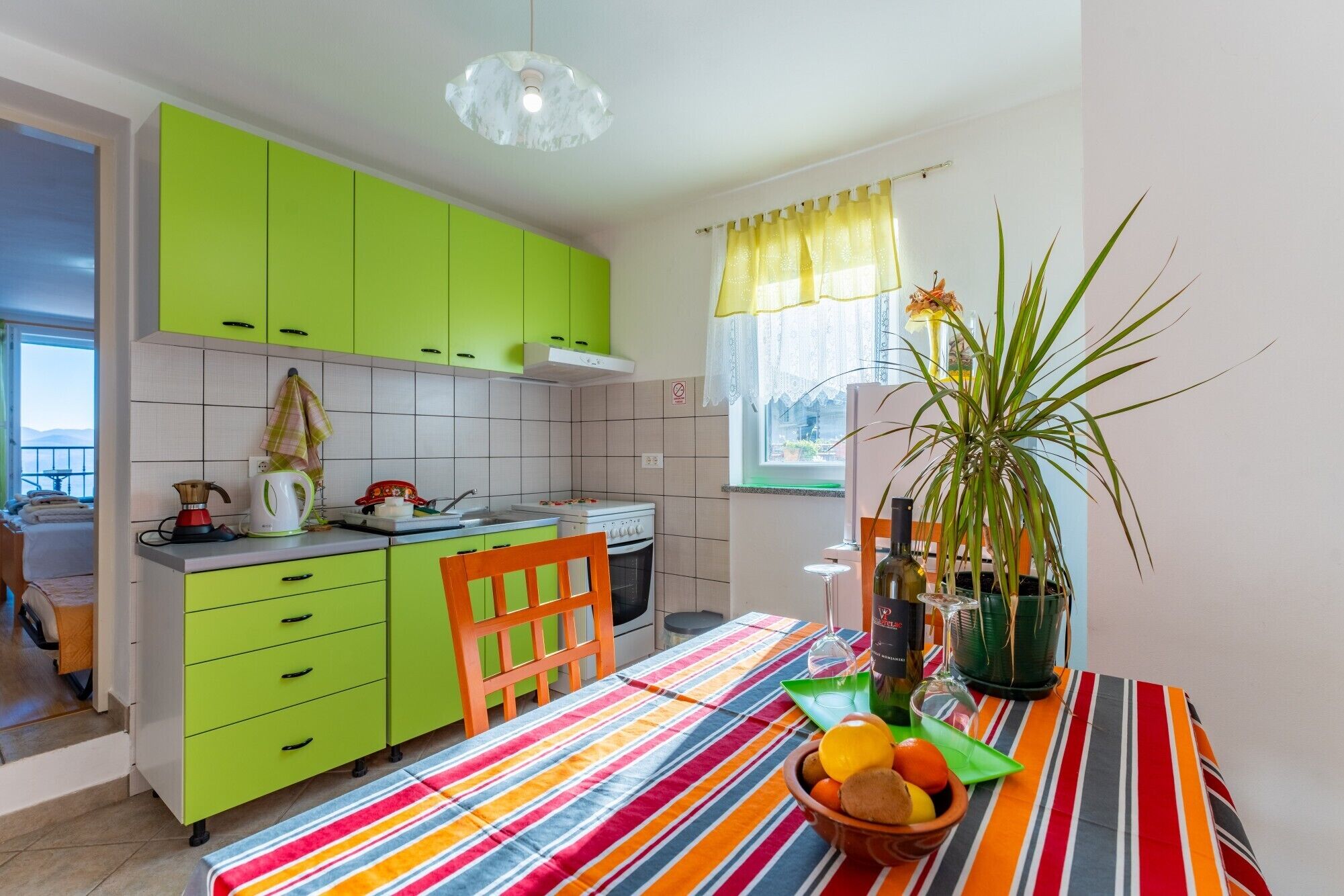 Una cocina con armarios verdes, un mantel a rayas y un tazón de fruta.