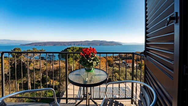 A balcony with a table and chairs, overlooking a scenic view of a body of water and distant hills.