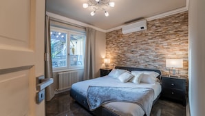 Un dormitorio moderno con una cama grande, un muro decorativo de piedra, una lámpara de techo y una ventana con cortinas.
