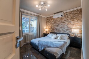 Un dormitorio moderno con una cama grande, un muro decorativo de piedra, una lámpara de techo y una ventana con cortinas.