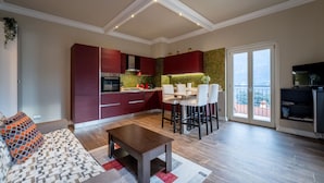 Una cocina moderna con armarios rojos, un comedor con sillas blancas y un balcón con vistas.
