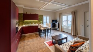 Una cocina moderna con armarios rojos, un comedor con mesa y sillas blancas, y una sala de estar con sofá y televisor.