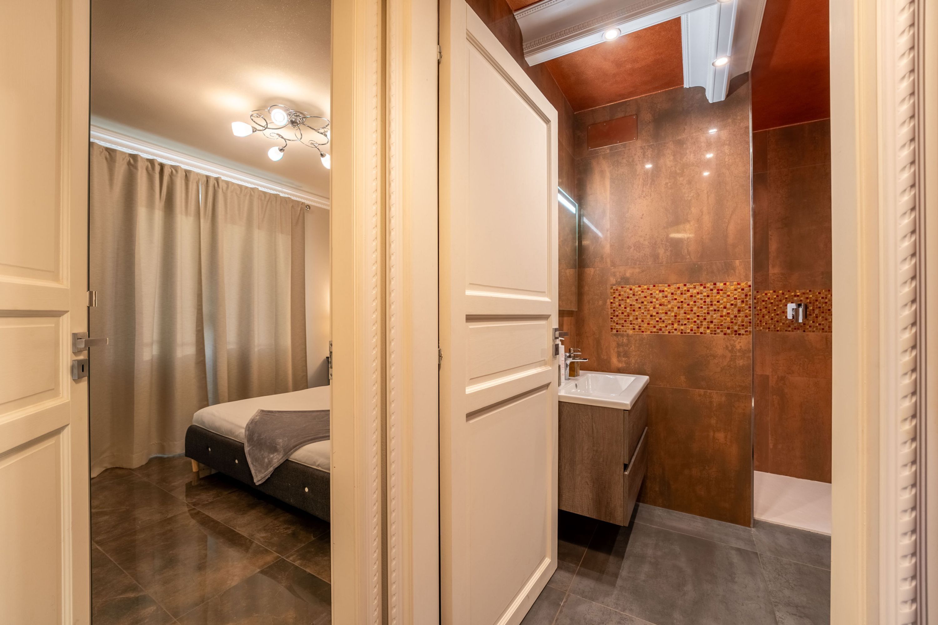 A bedroom with a bed, a bathroom with a sink and mirror, and a shower area.