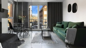 A modern living room with a green sofa, a glass dining table, and a view of the city through large windows. - Elite Apartments city center prestige (Gdansk)