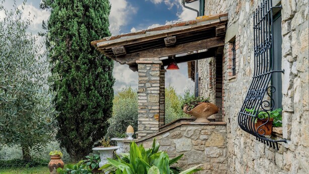 Un edificio de piedra con un balcón de madera, macetas con plantas y un gran árbol.