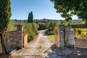 A stone pathway leading to a rustic stone building with a tiled roof, surrounded by greenery and trees.