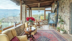 Una habitación acogedora con pared de piedra, techo de madera, zona de comedor con mesa y sillas, y un amplio ventanal con vistas panorámicas.