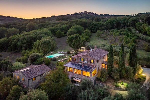 A hillside villa with a swimming pool, solar panels, and a view of the surrounding forest.