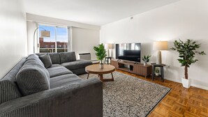 A modern living room with a sectional sofa, a round coffee table, a flat-screen TV, and two potted plants. - Gorgeous 2BR Next to BU y7k9 (Boston)