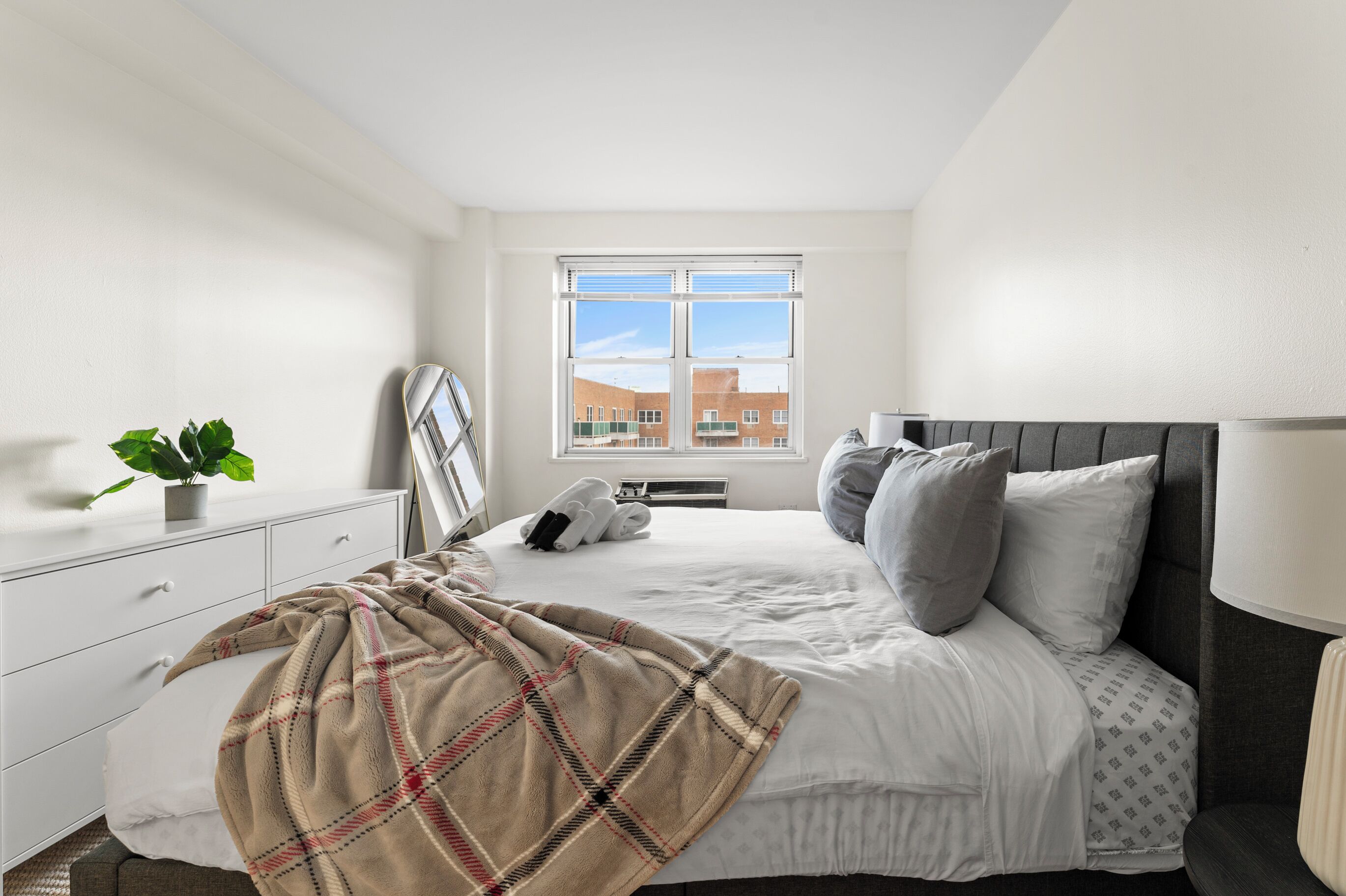 A bedroom with a bed, a bedside table, a window, and a potted plant.