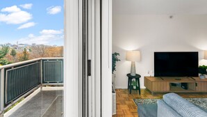 A balcony with a city view, a living room with a TV, and a sofa. - Beautiful 2BR Next to BU vcrs (Boston)