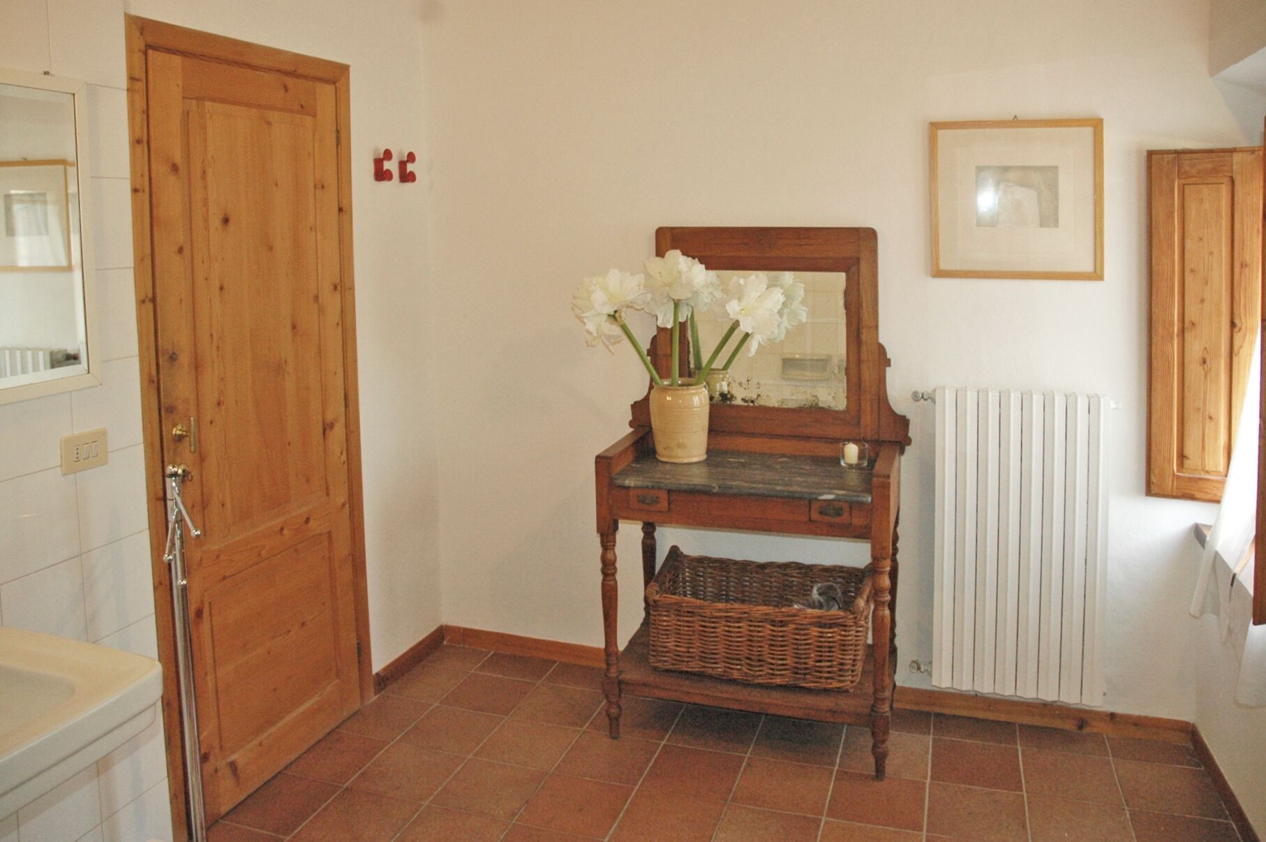 A wooden door, a mirror, a vase with flowers, a wicker basket, and a radiator.