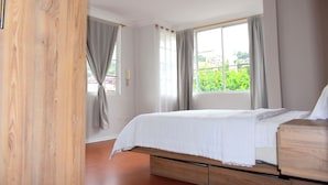A bedroom with a bed, wooden wardrobe, and a window with curtains.