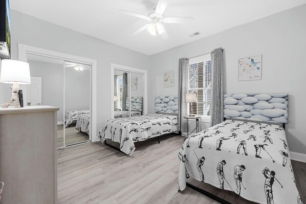 A bedroom with two beds, a ceiling fan, a bedside table, and a window with curtains.