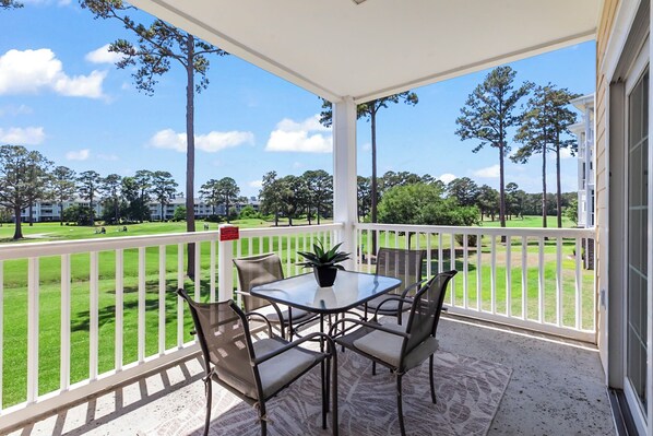 A covered patio with a table and chairs, overlooking a golf course.