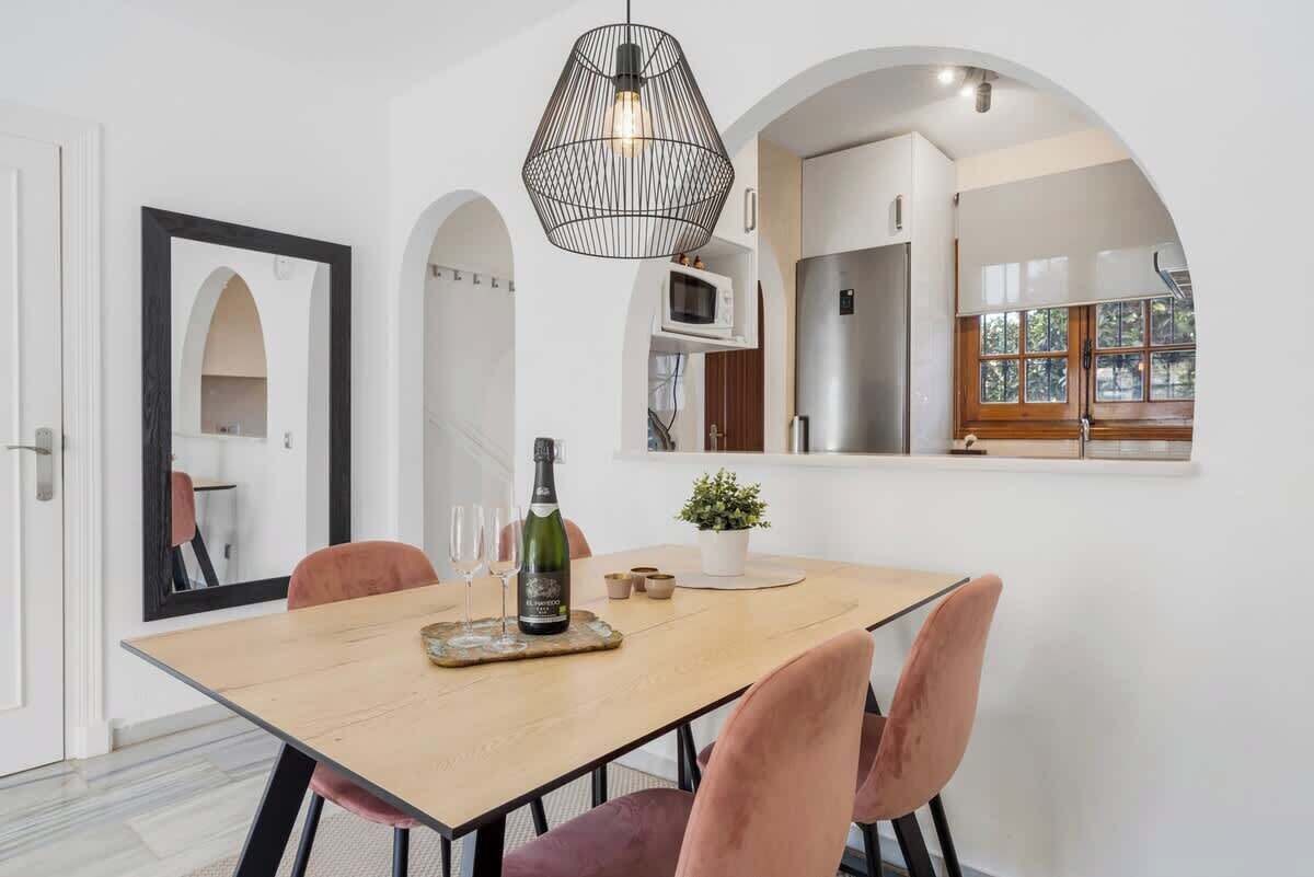 Een eethoek met een houten tafel, roze stoelen, een fles wijn en een kleine plant.