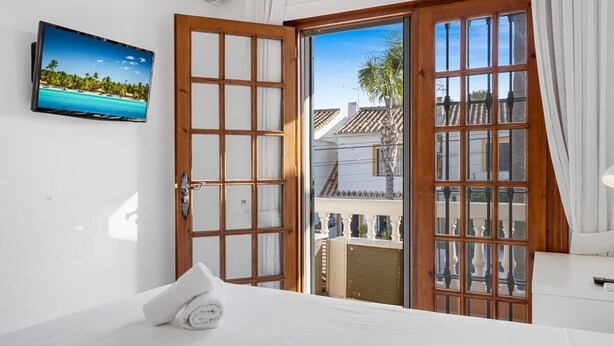 Een hotelkamer met een bed, een aan de muur bevestigde televisie en een grote glazen schuifdeur die leidt naar een balkon.
