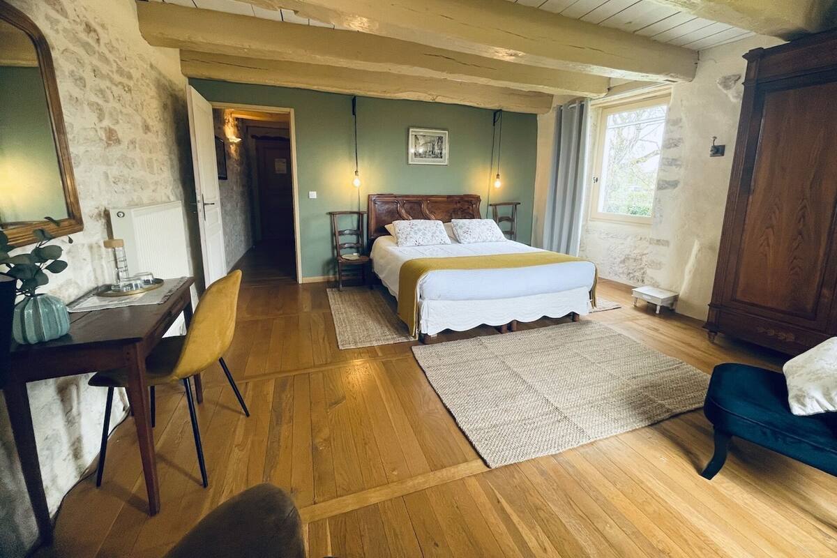 Une chambre à coucher avec un lit en bois, un bureau avec une chaise, une petite table et un placard.