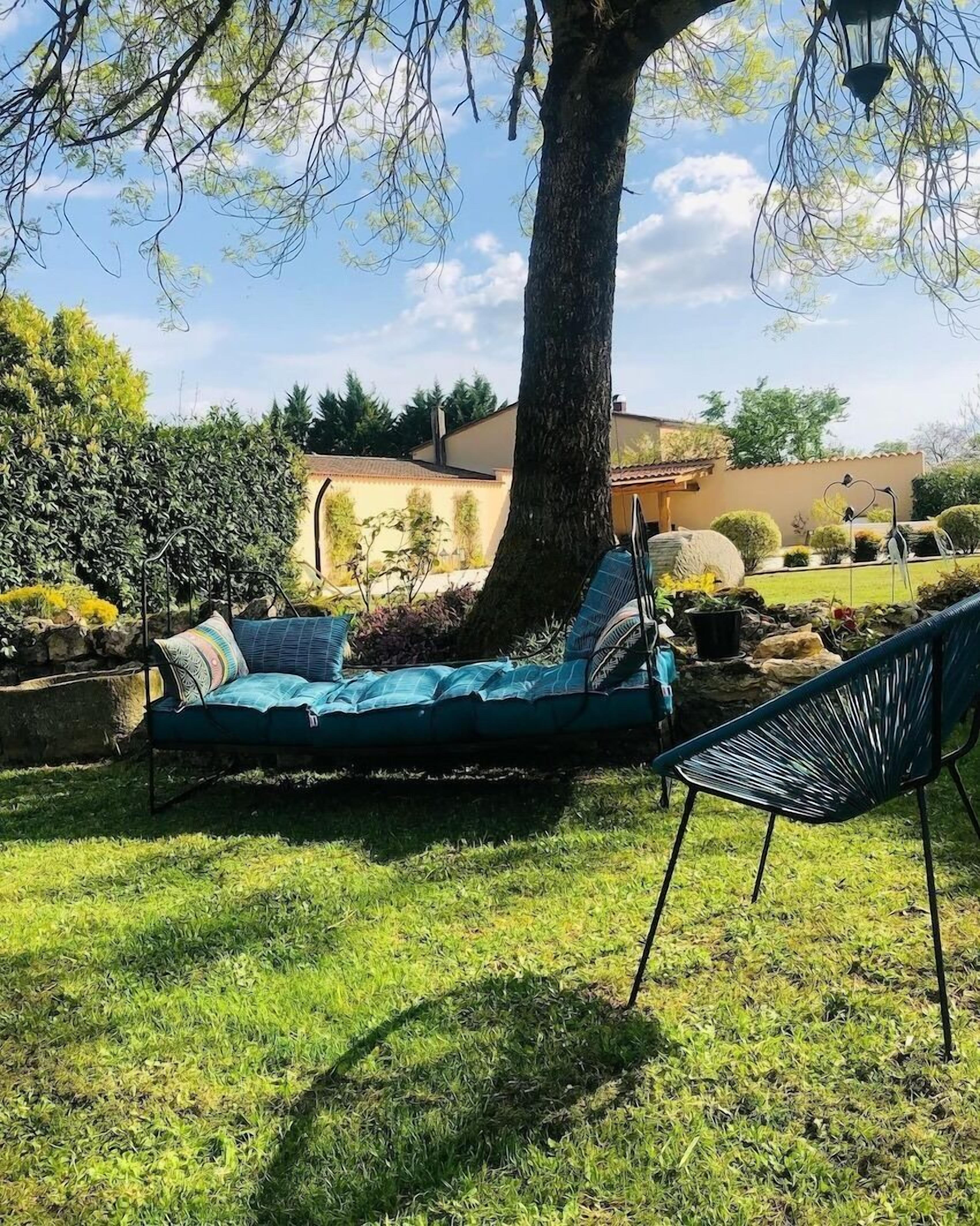 Eine Hängematte unter einem Baum, ein Stuhl und eine Steinmauer in einem Garten.