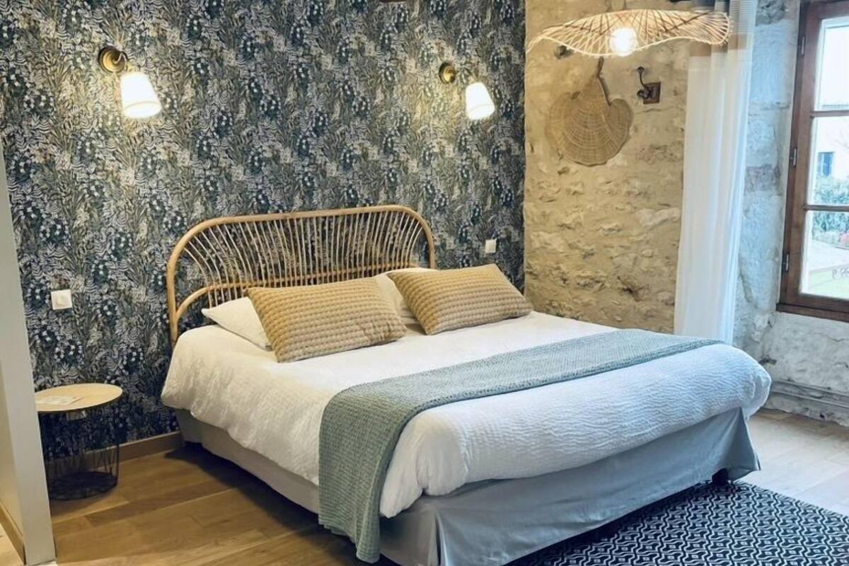 Une chambre à coucher avec un lit, une petite table de chevet, un tapis à motifs et un mur en pierre avec une fenêtre.