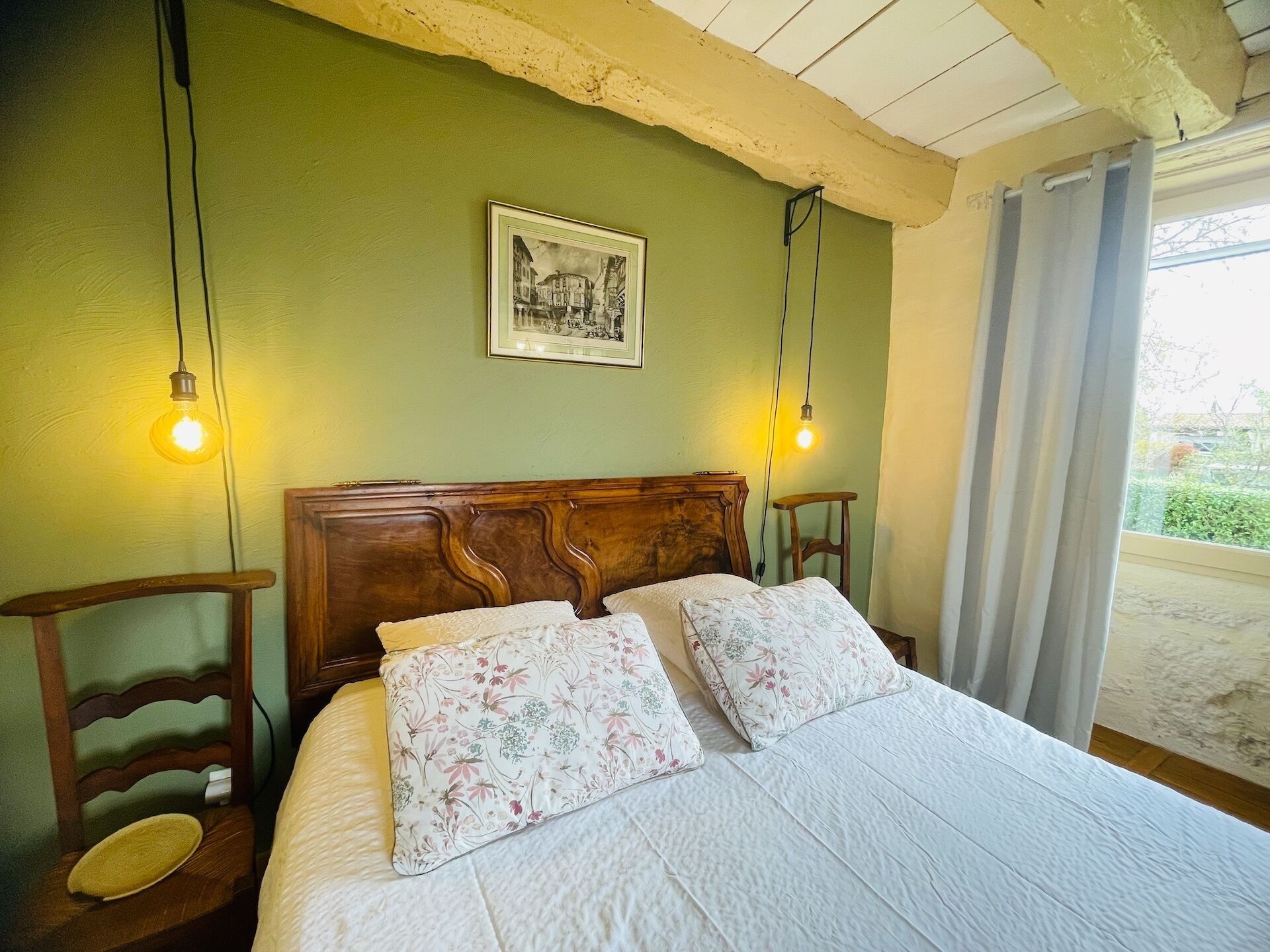 Quarto com cabeceira de madeira, duas almofadas florais, um quadro na parede e duas luminárias de mesa.