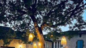 A stone building with a large tree in the center, outdoor seating, and hanging lights.