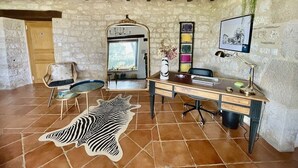 A rustic room with a stone wall, a wooden desk, a zebra rug, and a hanging plant.