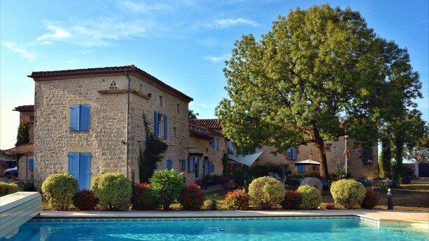 A stone building with a swimming pool, surrounded by well-maintained bushes and trees.