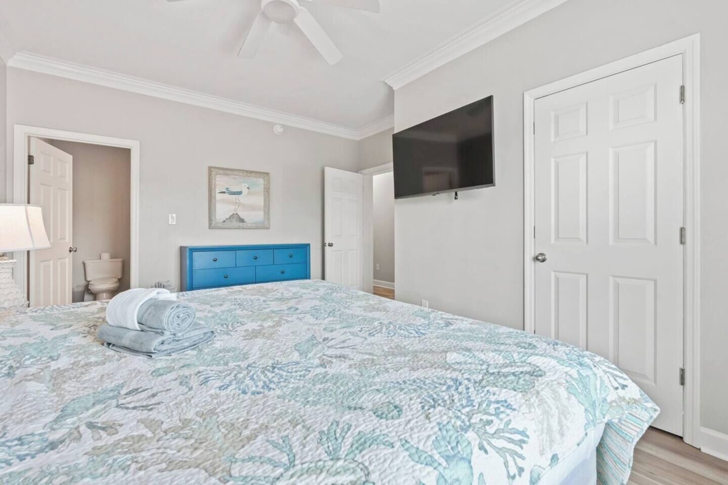 A bedroom with a bed, a blue dresser, a television on the wall, and a door.