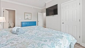 Une chambre à coucher avec un lit, une commode bleue, un téléviseur fixé au mur et une porte.