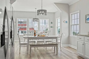 A modern kitchen with white cabinetry, a stainless steel refrigerator, and a dining area with a white table and chairs.