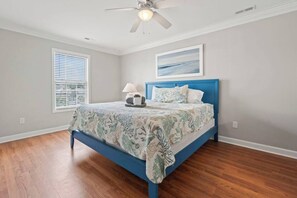 Une chambre à coucher avec un lit, un ventilateur de plafond, une fenêtre avec des stores et un tableau accroché au mur.
