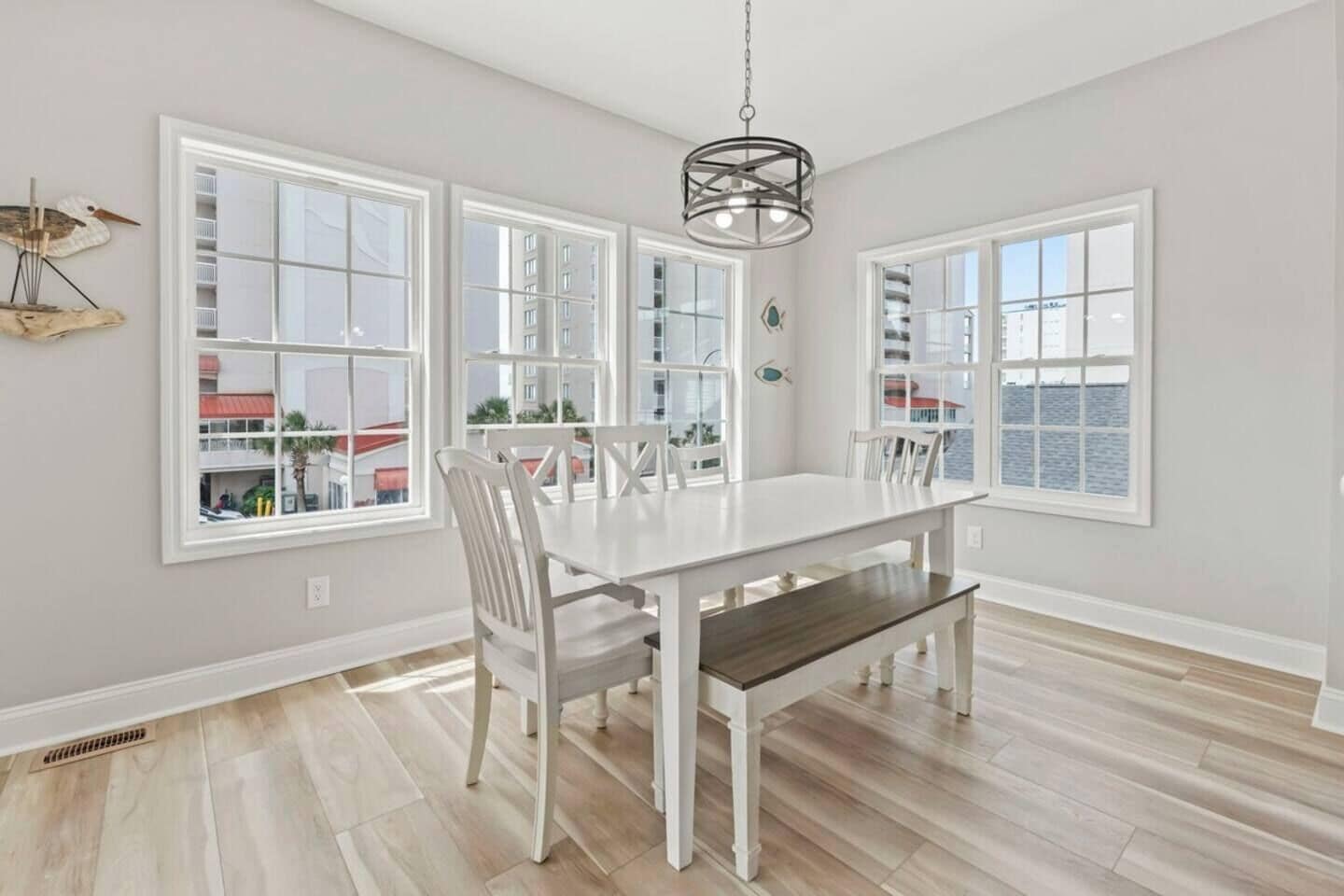 A dining area with a white table and chairs, large windows, and a hanging light fixture.