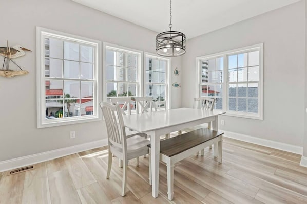 A dining area with a white table and chairs, large windows, and a hanging light fixture.