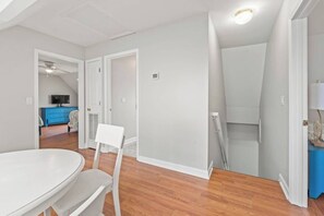Une pièce avec une table à manger blanche, des chaises, un buffet bleu et un téléviseur à l’arrière-plan.