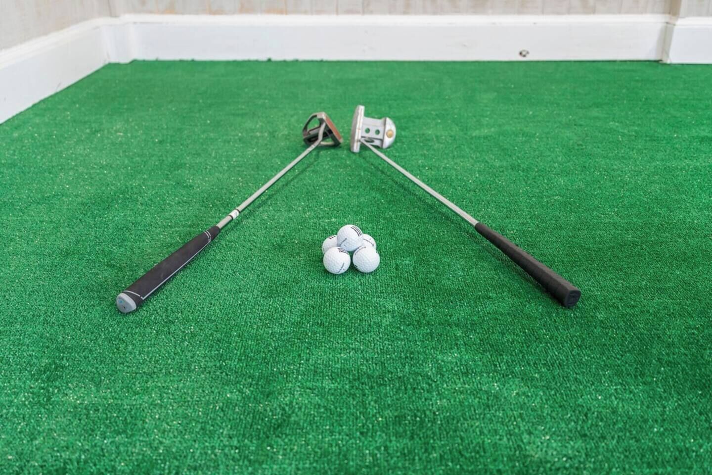 A green artificial turf surface with two golf clubs and a small pile of golf balls.