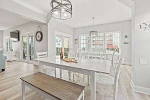 A spacious dining area with a white table set for four, surrounded by white chairs, and a bench.