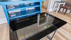 A modern kitchen with a glass-top table displaying a digital screen, a blue storage unit, and a wooden floor. - Epic 7BR Getaway - Pool, Game Room, Put-put, Beach (North Myrtle Beach)
