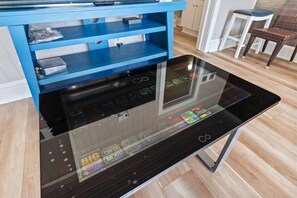 A modern kitchen with a glass-top table displaying a digital screen, a blue storage unit, and a wooden floor. - Epic 7BR Getaway - Pool, Game Room, Put-put, Beach (North Myrtle Beach)