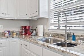 A kitchen with white cabinets, a granite countertop, a double sink, and a window with blinds. - Epic 7BR Getaway - pool, game room, put-put, beach (North Myrtle Beach)