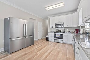 Une cuisine moderne dotée d’appareils électroménagers en acier inoxydable, de meubles blancs et d’un plancher en bois.