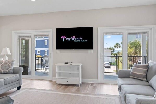 A living room with a flat-screen TV mounted on the wall, a sofa, a coffee table, and a TV stand. - Epic 7BR Getaway - pool, game room, put-put, beach (North Myrtle Beach)