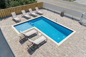 A rectangular swimming pool with a tiled deck, surrounded by white metal chairs. - Epic 7BR Getaway - pool, game room, put-put, beach (North Myrtle Beach)