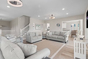 A spacious living room with a neutral color palette, a staircase, and a kitchen area visible through an open doorway. - Epic 7BR Getaway - Pool, Game Room, Put-put, Beach (North Myrtle Beach)
