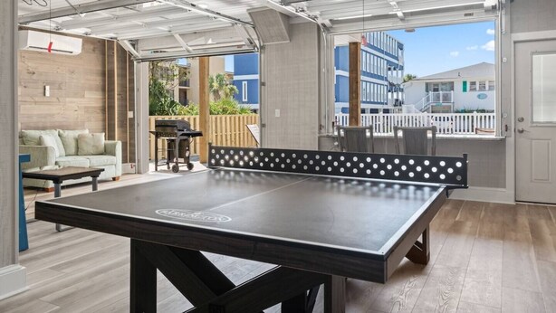 A ping pong table in a room with a view of a building outside. - Epic 7BR Getaway - Pool, Game Room, Put-put, Beach (North Myrtle Beach)