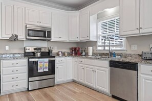 A kitchen with white cabinets, a stainless steel oven, a microwave, a coffee maker, and a dishwasher. - Epic 7BR Getaway - pool, game room, put-put, beach (North Myrtle Beach)