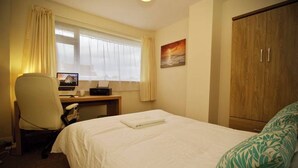A hotel room with a bed, a desk with a computer, a chair, a wardrobe, and a window with curtains. - Ringswell Gardens Room 3 Queen (Bath)